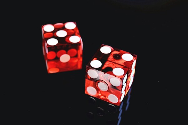 Two transparent red dice with white dots on a glossy black surface, casting soft reflections.